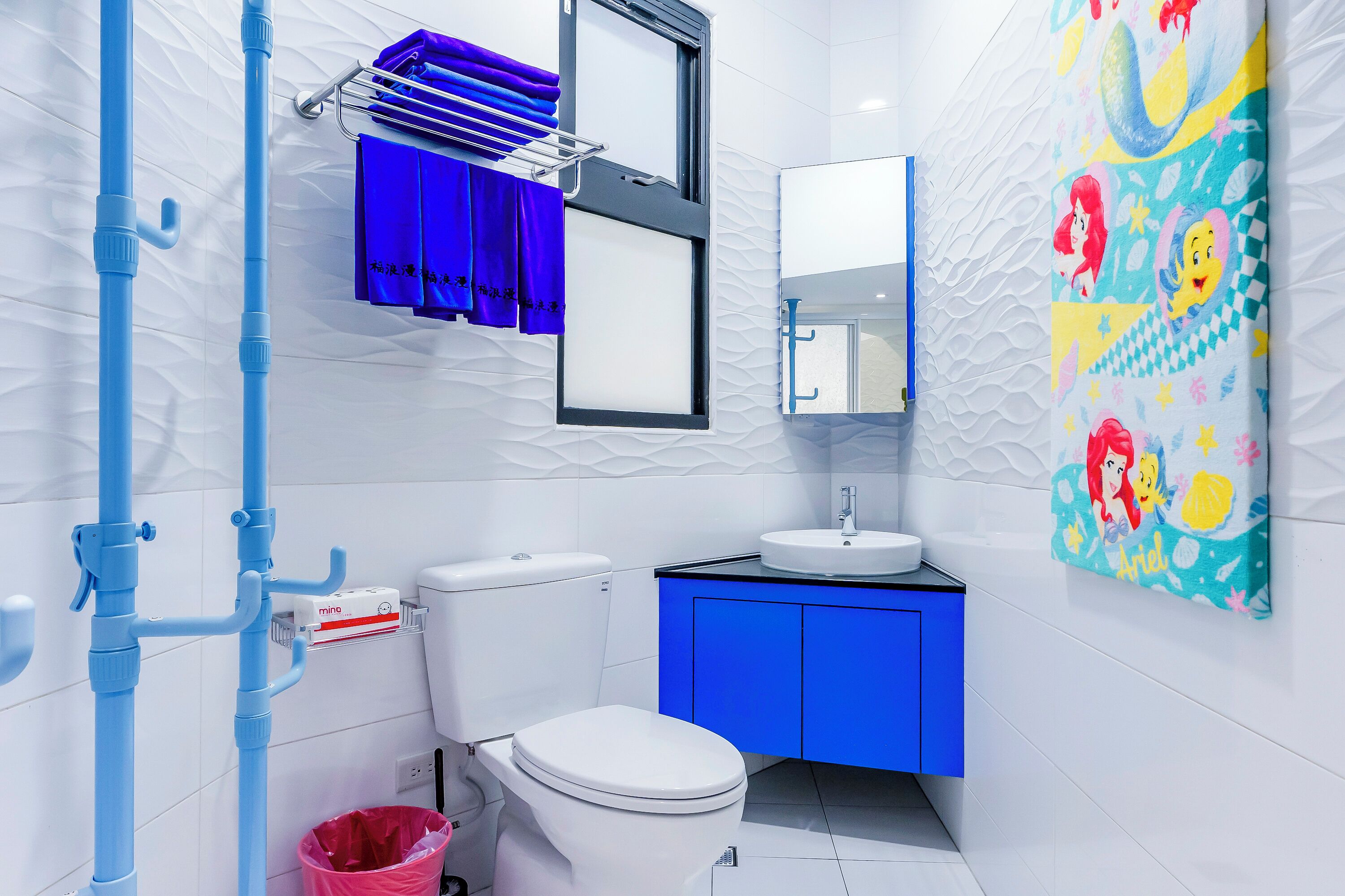 Un baño moderno con inodoro blanco, mueble azul y una obra de arte colorida en la pared.