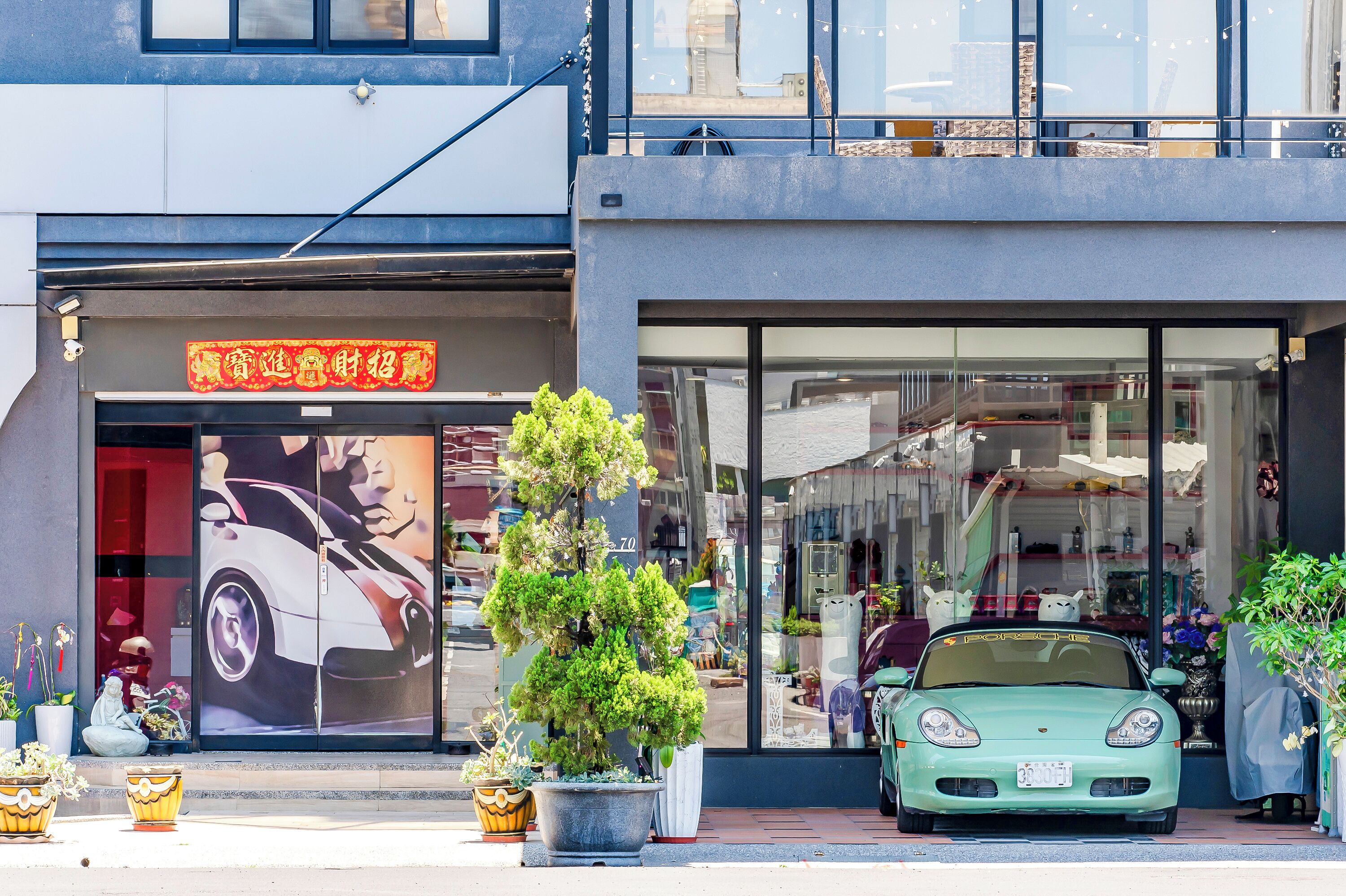 A storefront with a large car window display, potted plants, and a parked car.