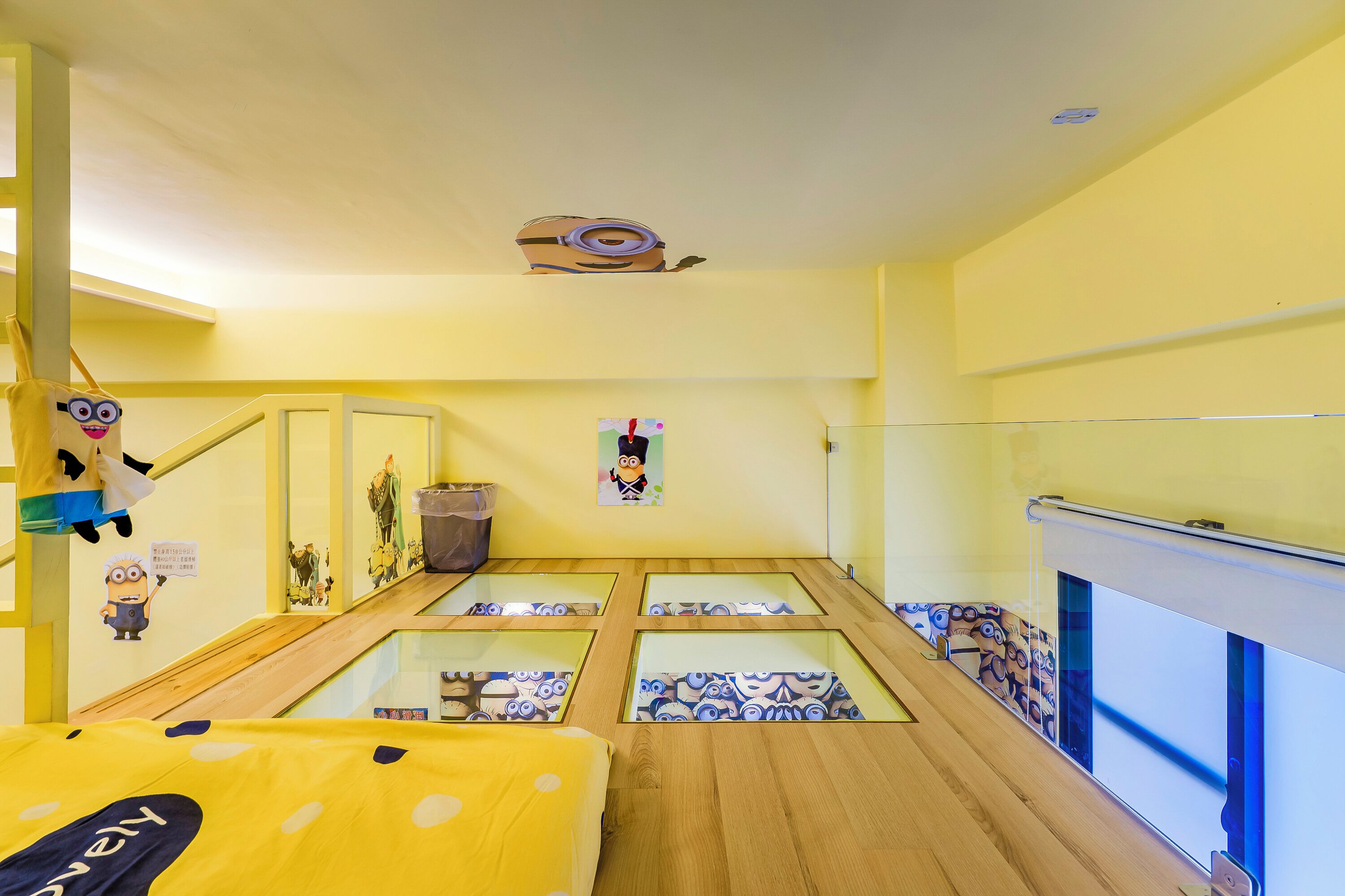 Een kamer in geel decor, met een bed met een gele stippenhoes, een klein bureau en een raam met uitzicht op buiten.