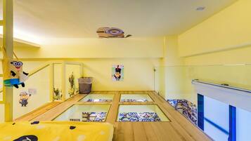 Een kamer in geel decor, met een bed met een gele stippenhoes, een klein bureau en een raam met uitzicht op buiten.
