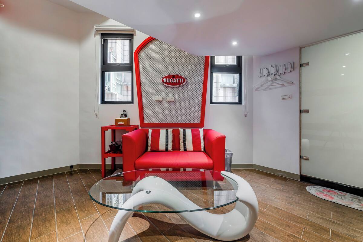 Ein modernes Wohnzimmer mit einem roten Sofa, einem Glastisch und einem an der Wand befestigten Bugatti-Logo.