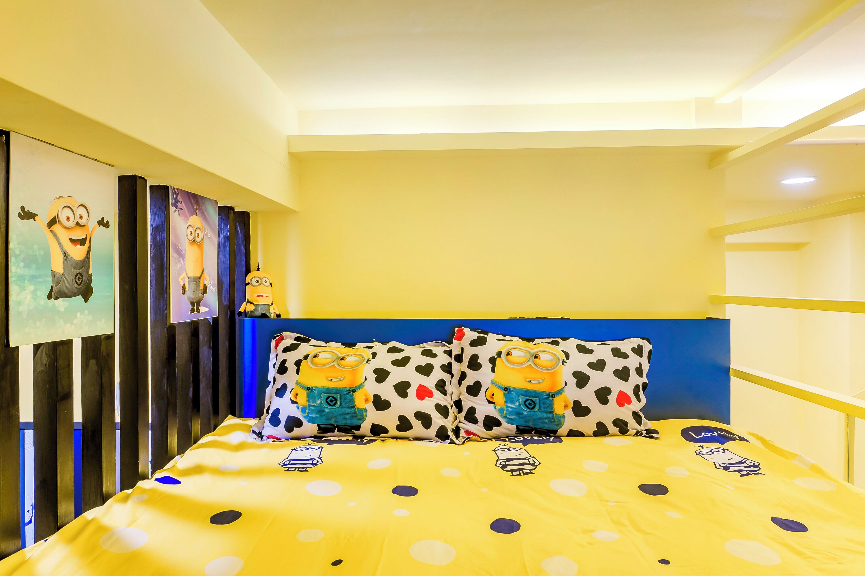 A room with a bed featuring a yellow polka dot bedspread, two pillows with Minion designs, and a blue headboard.