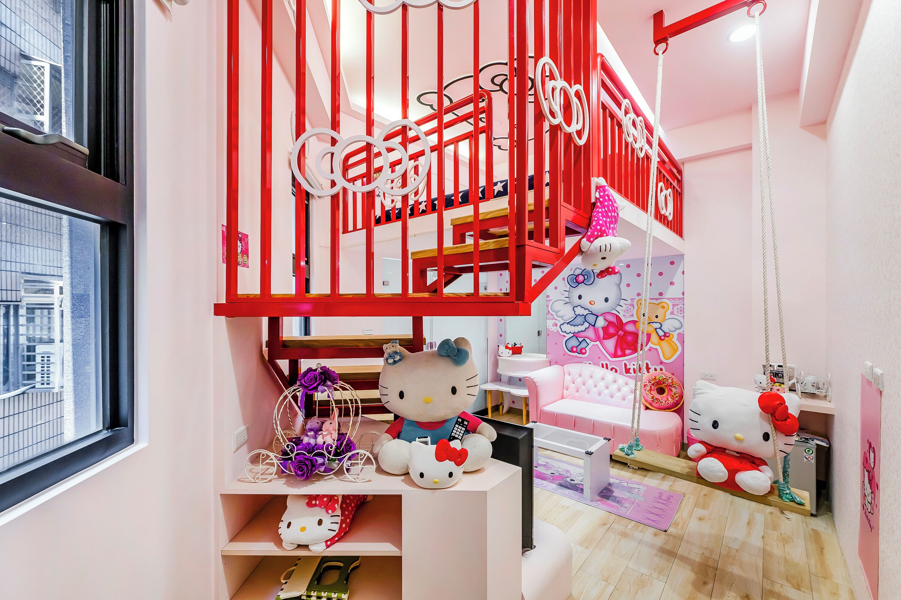 Zona de juegos infantiles con decoración de Hello Kitty, un columpio y una escalera con barandillas rojas.