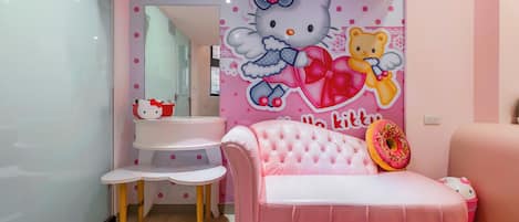 Una habitación decorada en tonos rosas, con un mural de Hello Kitty en la pared, un sofá rosa, una pequeña mesa blanca y una silla rosa.