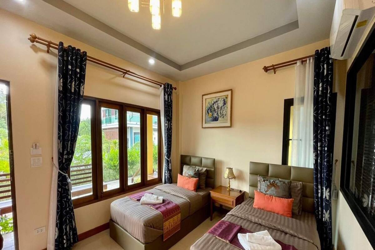 A hotel room with two beds, a large window, a ceiling fan, and a painting on the wall.