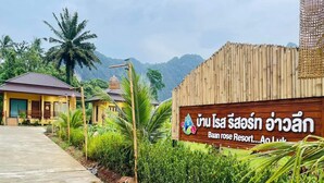 A resort sign with a logo and text in a foreign language, surrounded by lush greenery and a clear sky. - Capital O 75518 Baan Rose Resort Ao Luk (Ao Luek)