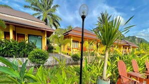 A tropical resort with two yellow buildings, a paved deck, and lush greenery. - Capital O 75518 Baan Rose Resort Ao Luk (Ao Luek)