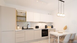 Une cuisine moderne avec des meubles blancs, un plan de travail en marbre, un four encastré et un coin repas comprenant une table et des chaises blanches.