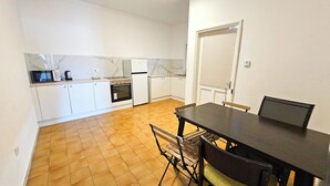 A compact kitchen with white cabinets, a built-in oven, and a microwave. There's a dining table with chairs and a bench. - Downtown Rooms, 200m from Marina Beach (Larnaca)