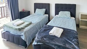 A hotel room with two beds, a painting of a sunset, a window with curtains, and a view of a building outside. - Downtown Rooms, 200m from Marina Beach (Larnaca)