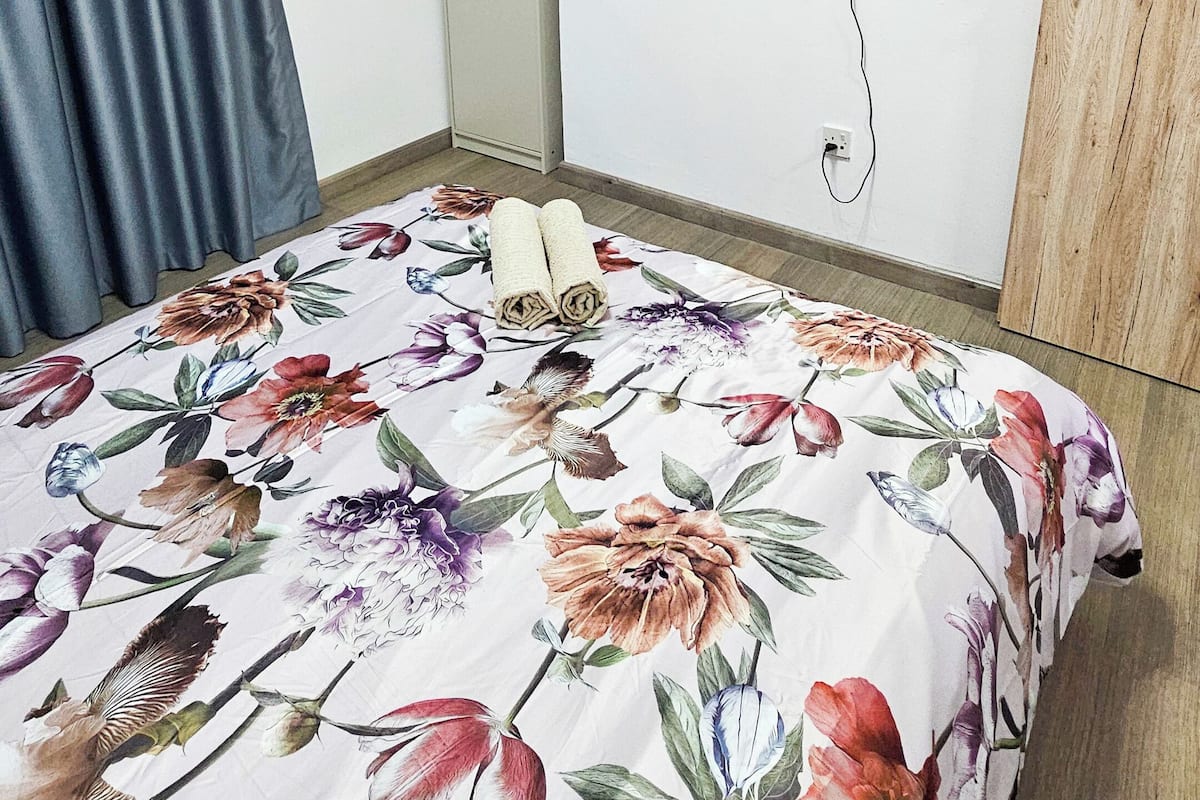 Quarto com uma cama, televisão na parede, porta de madeira e cortina.