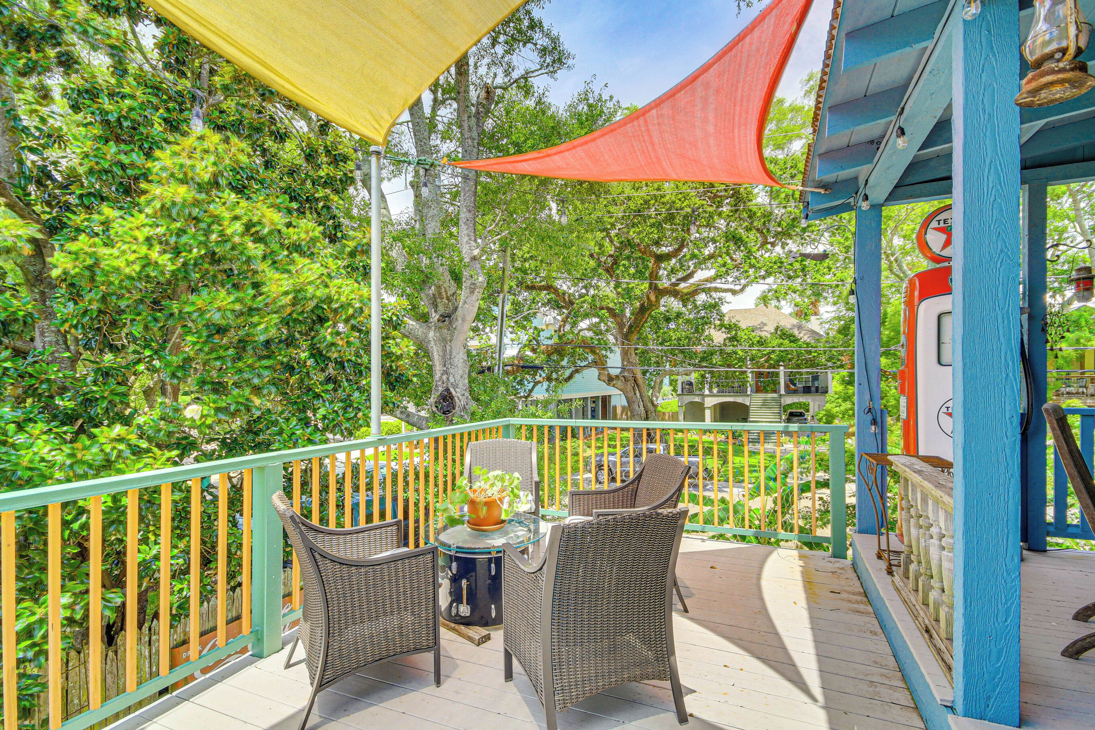A balcony with wicker chairs and a small table, surrounded by a wooden railing and a yellow shade.