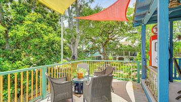 A balcony with wicker chairs and a small table, surrounded by a wooden railing and a yellow shade.