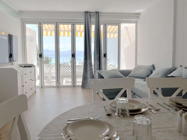 Un comedor moderno con una mesa preparada para cuatro, un sofá y un televisor en la pared.