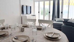 A dining area with a round table set for four, a sofa, and a TV in the background. - Beachfront · Terrace · Adults Only (Alcudia - Puerto de Alcudia)