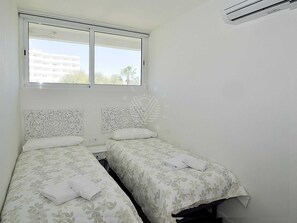 Une petite chambre propre, avec deux lits, une fenêtre et un appareil de climatisation.