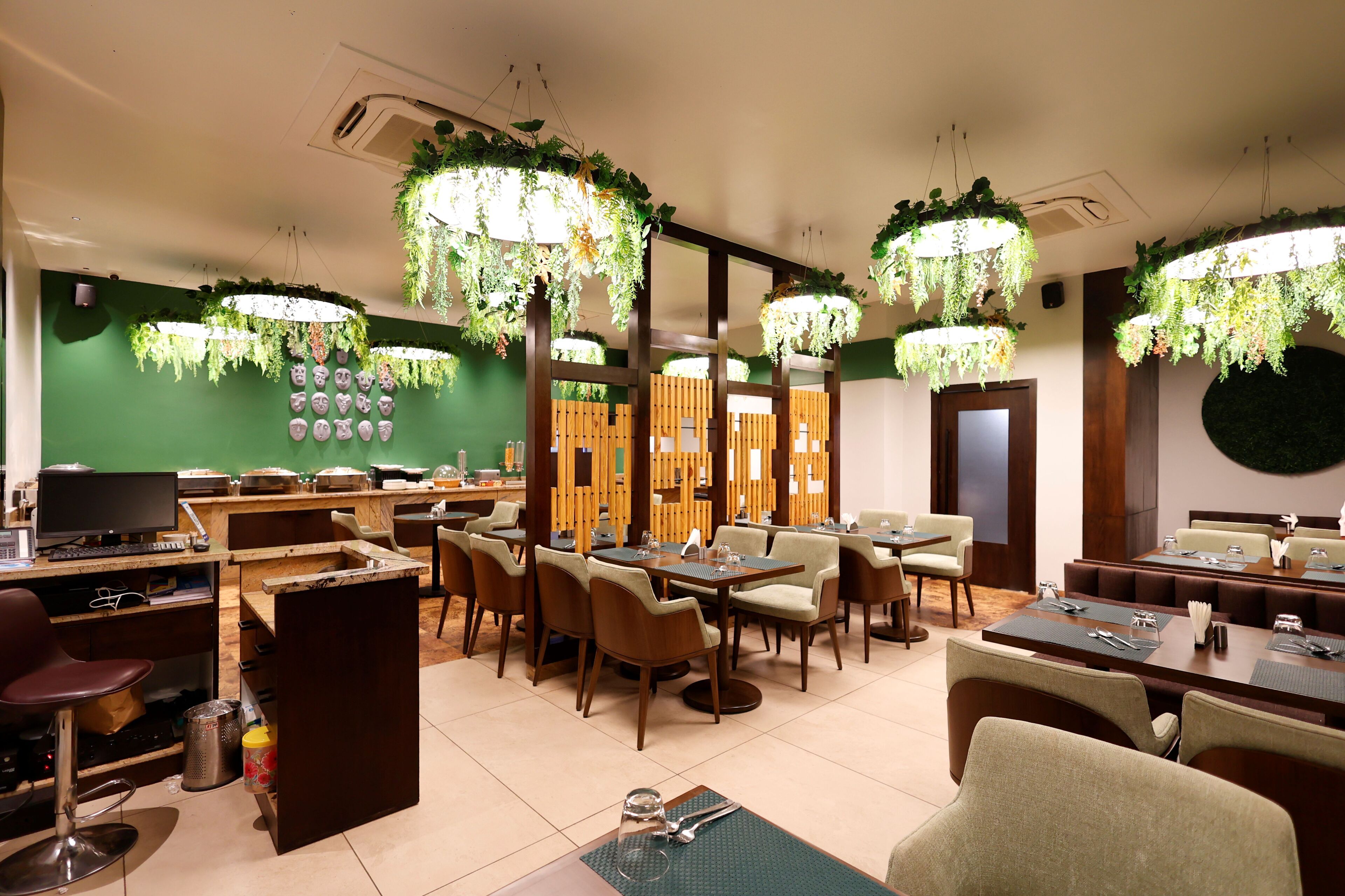 A restaurant with multiple dining tables and chairs, hanging plants, and a green wall with decorative items.