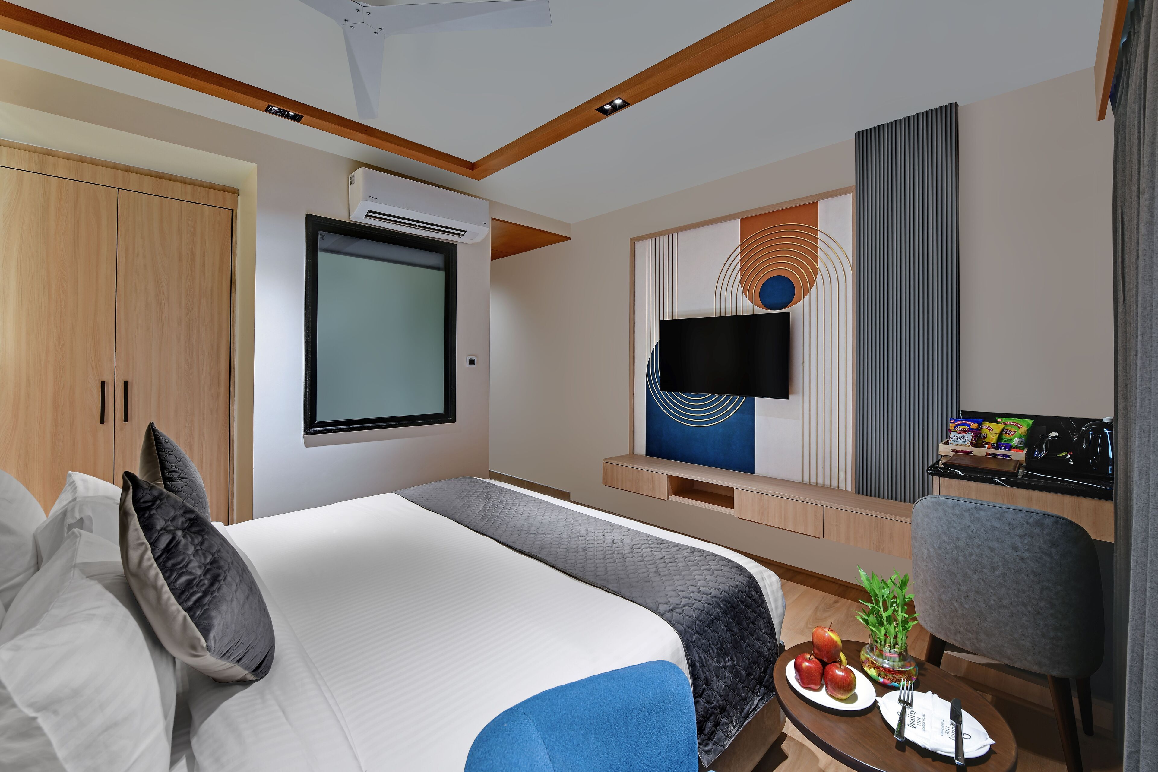A modern hotel room with a large bed, a flat-screen TV, a small kitchenette, and a dining area.