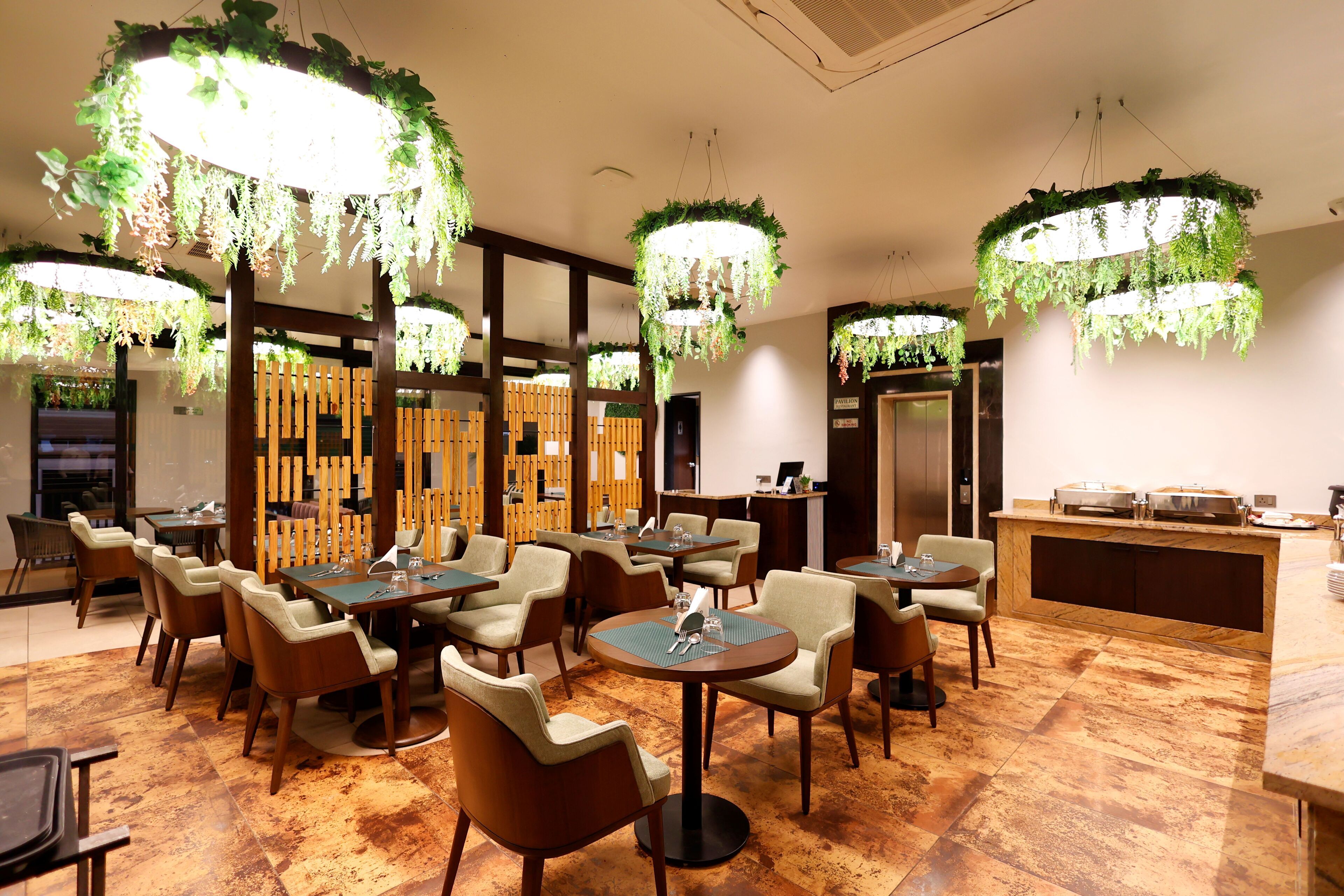 A restaurant with round tables and chairs, hanging plants, and a wooden partition.