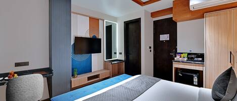 Una habitación de hotel con cama, escritorio, silla, televisor y kitchenette.