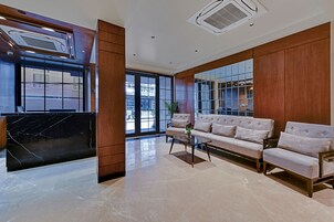 A modern lobby with a marble reception desk, a sofa set, and large windows offering a view of the city.