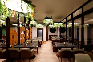 Un restaurante con varias mesas y sillas, separadores de madera y plantas colgantes.