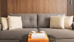 Een moderne woonkamer met een grijze bank, twee wandlampen en een bijzettafel met een Louis Vuitton catalogus.
