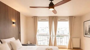 Een hotelkamer met een bed, een plafondventilator, een raam met gordijnen en een radiator.