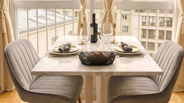 Een eettafel gedekt voor twee personen, met een fles wijn, glazen en een mand met brood.