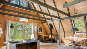 Un loft espacioso con techo alto, vigas de madera, chimenea, comedor y grandes ventanales que ofrecen vistas al exterior.