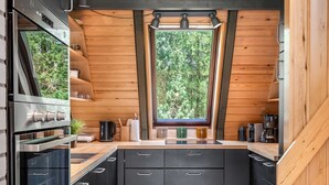 Cocina compacta con una isla central, paredes de madera y ventana con vistas a la vegetación.