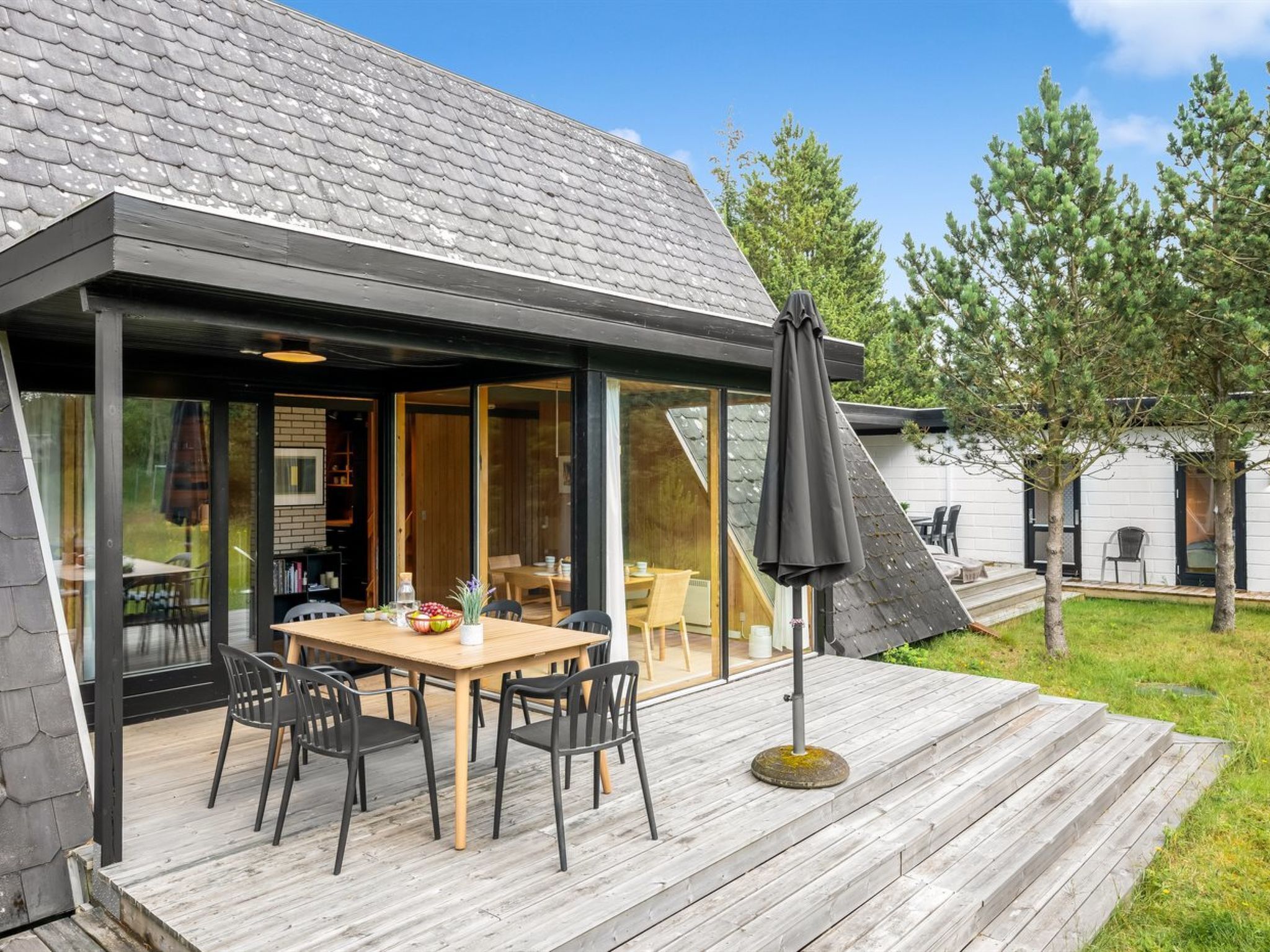 A modern house with a covered patio, a dining table with chairs, and a large umbrella.