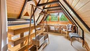 Un dormitorio acogedor en el ático con cama elevada, vigas de madera, un escritorio y una silla.