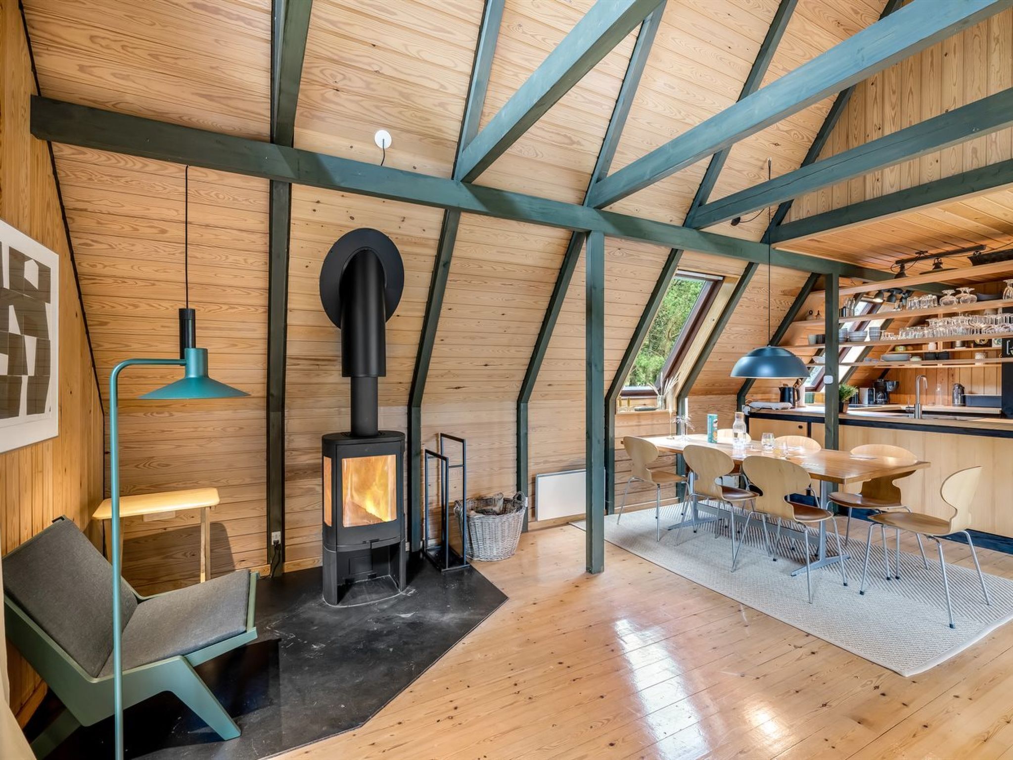 Un loft moderno y acogedor con una estufa de leña central, un comedor con vistas y una cocina con estantes de madera.