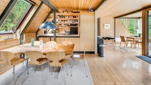 Un interior moderno con un área de comedor de madera, una cocina con estantes de madera y un gran ventanal que ofrece vistas al exterior.