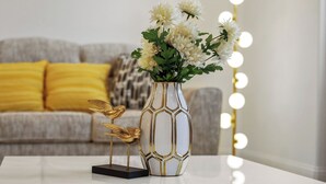 En hvid vase med geometrisk mønster, en gylden fugleskulptur og en buket hvide blomster på et hvidt bord.