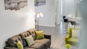 A modern living room with a brown leather sofa, green and patterned cushions, a glass coffee table, and a floor lamp. - Tranquil 3BR I Free Parking I Workspace (Grand Prairie)