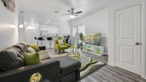 A modern living room with a grey sofa, a green armchair, and a TV on a white cabinet. - Tranquil 3BR I Free Parking I Workspace (Grand Prairie)