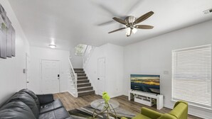 A modern living room with a black leather couch, a green armchair, a glass coffee table, a flat-screen TV, and a ceiling fan. - Tasteful 3BR I Free Parking I Workspace (Grand Prairie)