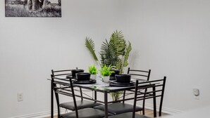 A dining area with a table set for four, surrounded by chairs, with a plant centerpiece and a wall-mounted light fixture above. - Tasteful 3BR I Free Parking I Workspace (Grand Prairie)