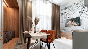 A modern dining area with a table set for two, a sofa, and a wall-mounted TV. - Qult·co - Legends of the Fall (București)