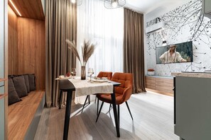 A modern dining area with a wooden bench, a table set for two, and a large TV on the wall.