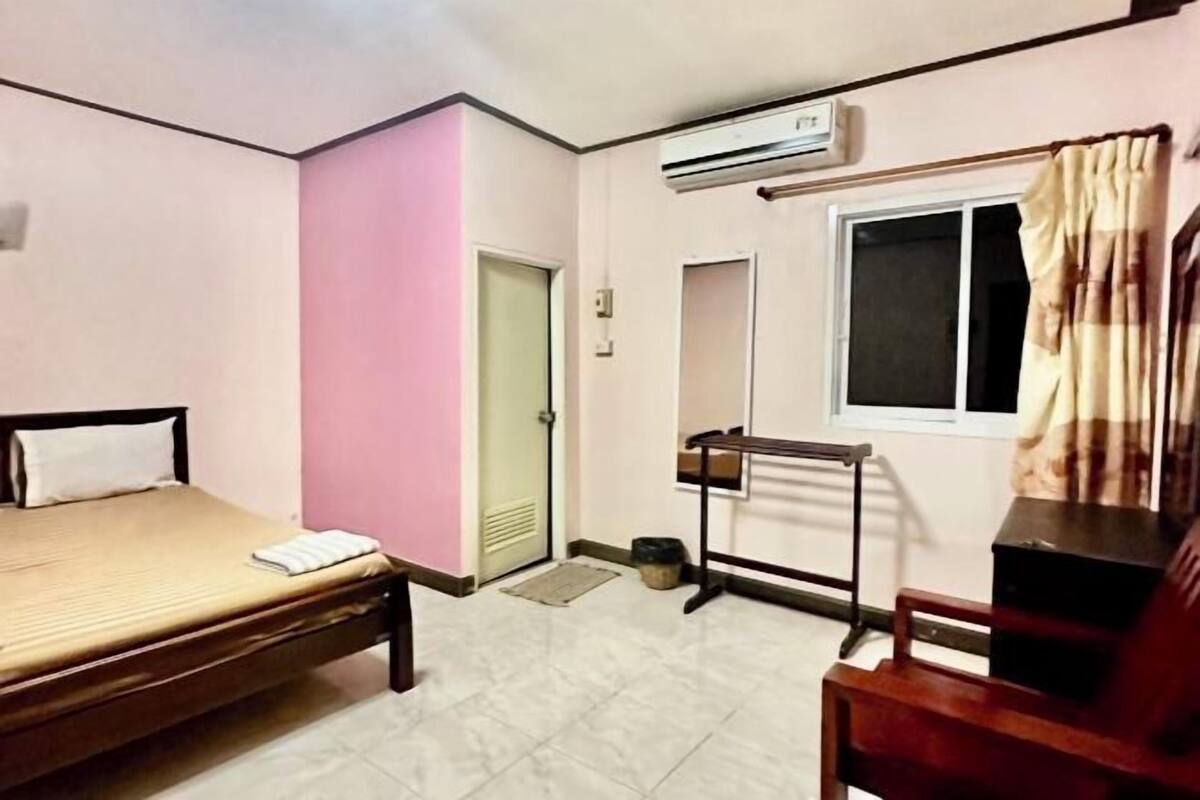 A room with a bed, a desk, a chair, an air conditioning unit, a window with curtains, and a door.