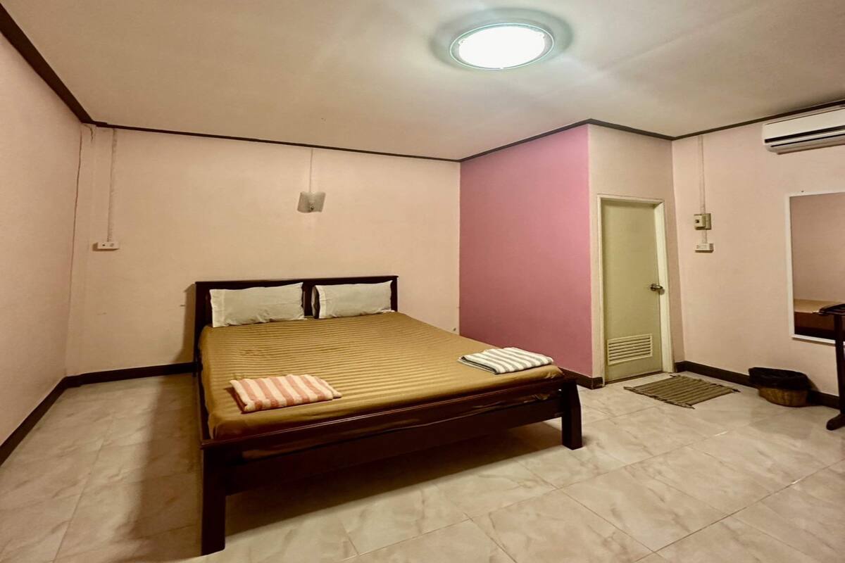 A small, neatly arranged bedroom with a single bed, a door, and an air conditioning unit.