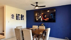 Un coin repas comprenant une table et des chaises, un ventilateur de plafond et un téléviseur à écran plat fixé au mur.