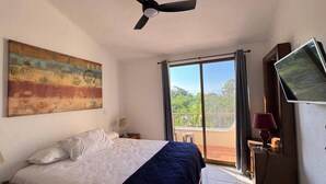 Une chambre avec un lit, un ventilateur de plafond, une télévision et un balcon avec vue.