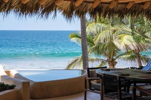 A beachside lounge with a view of the ocean, palm trees, and a thatched roof.