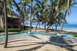 A pool with a curved edge, surrounded by palm trees and a beach view.