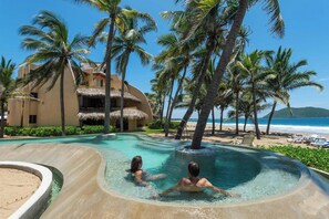 A resort pool with two people, surrounded by palm trees and a beach view.