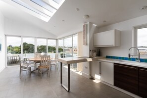 A modern kitchen with a dining area, large windows, and a view of the city. - Spacious House nr Castle Beach, Parking & Sauna (Cornwall)